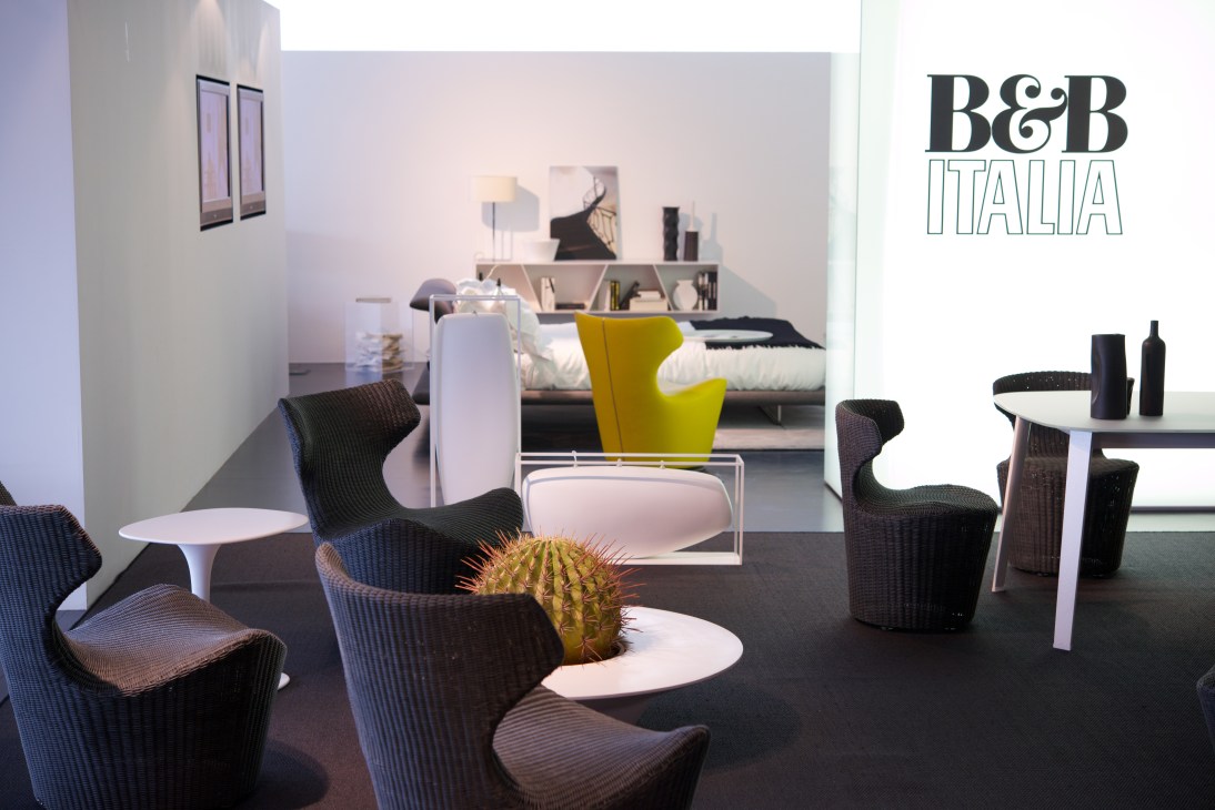 B&B Italia showroom displaying modern furniture including curved dark chairs, white tables, and a yellow chair with shelving and bed in background.