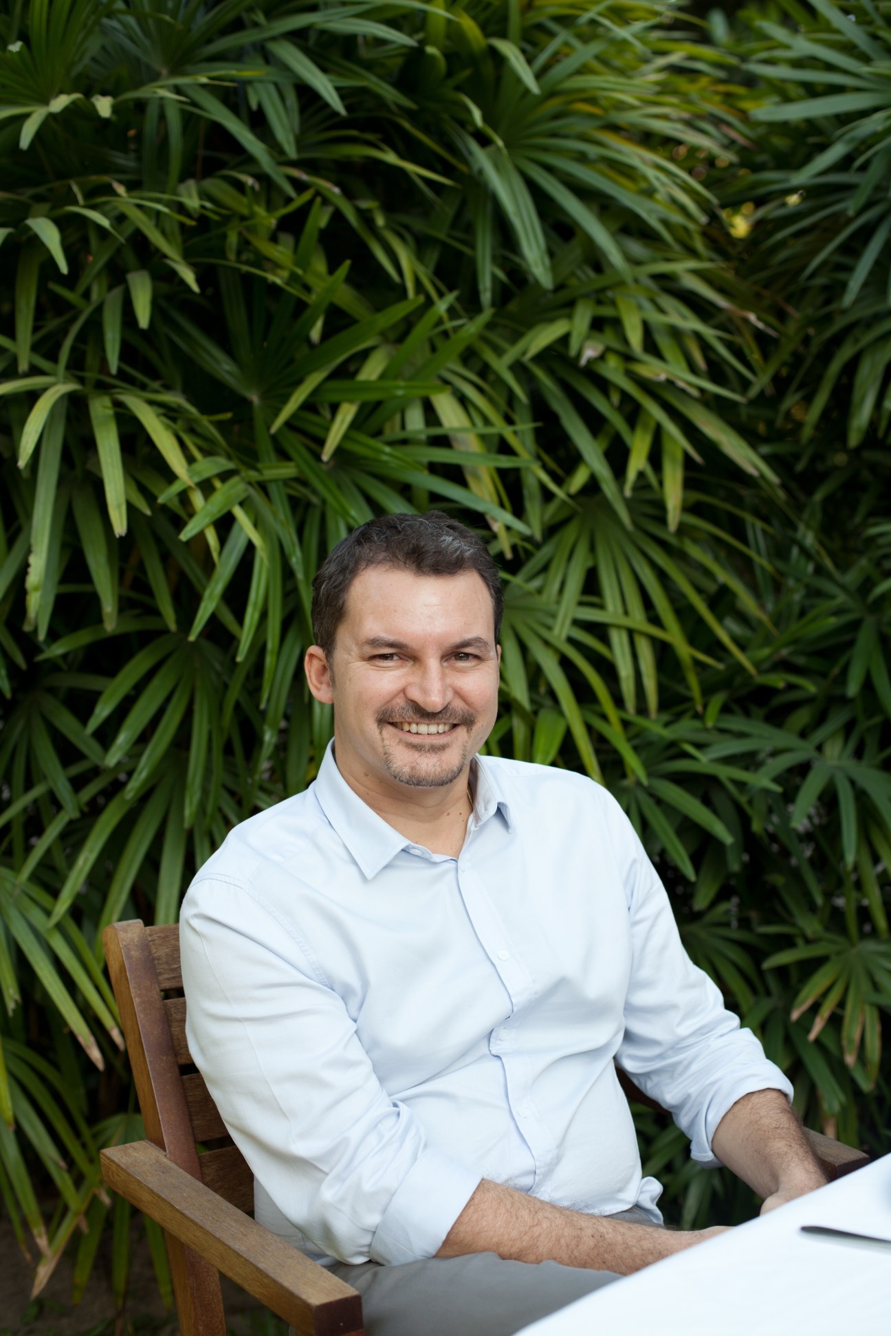 François Stoupan, owner of Shwe Sa Bwe restaurant, smiling at the camera in front of green foliage.