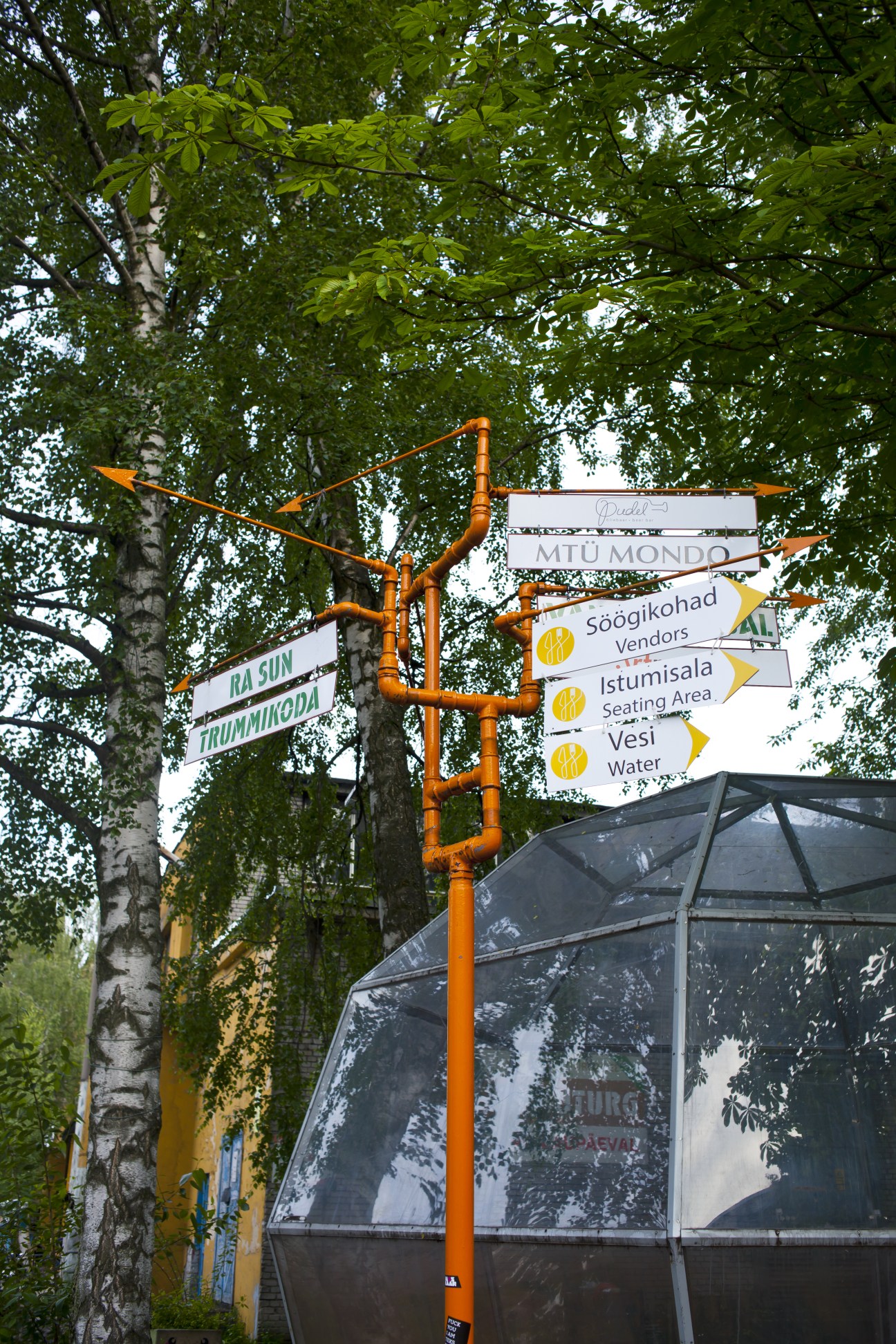 Orange directional signpost with Estonian wayfinding signs among green tree foliage in Kalamaja.