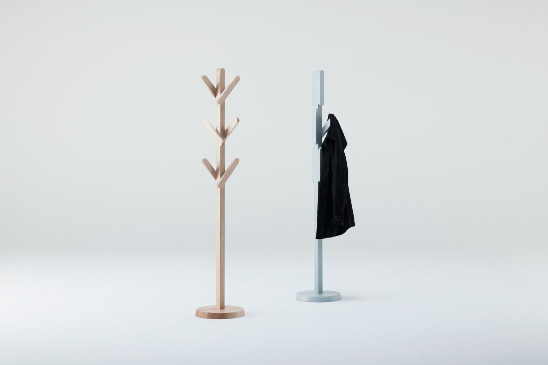 Two minimalist coat stands—one wooden with branch-like hooks, one blue-grey metal—against a white background.