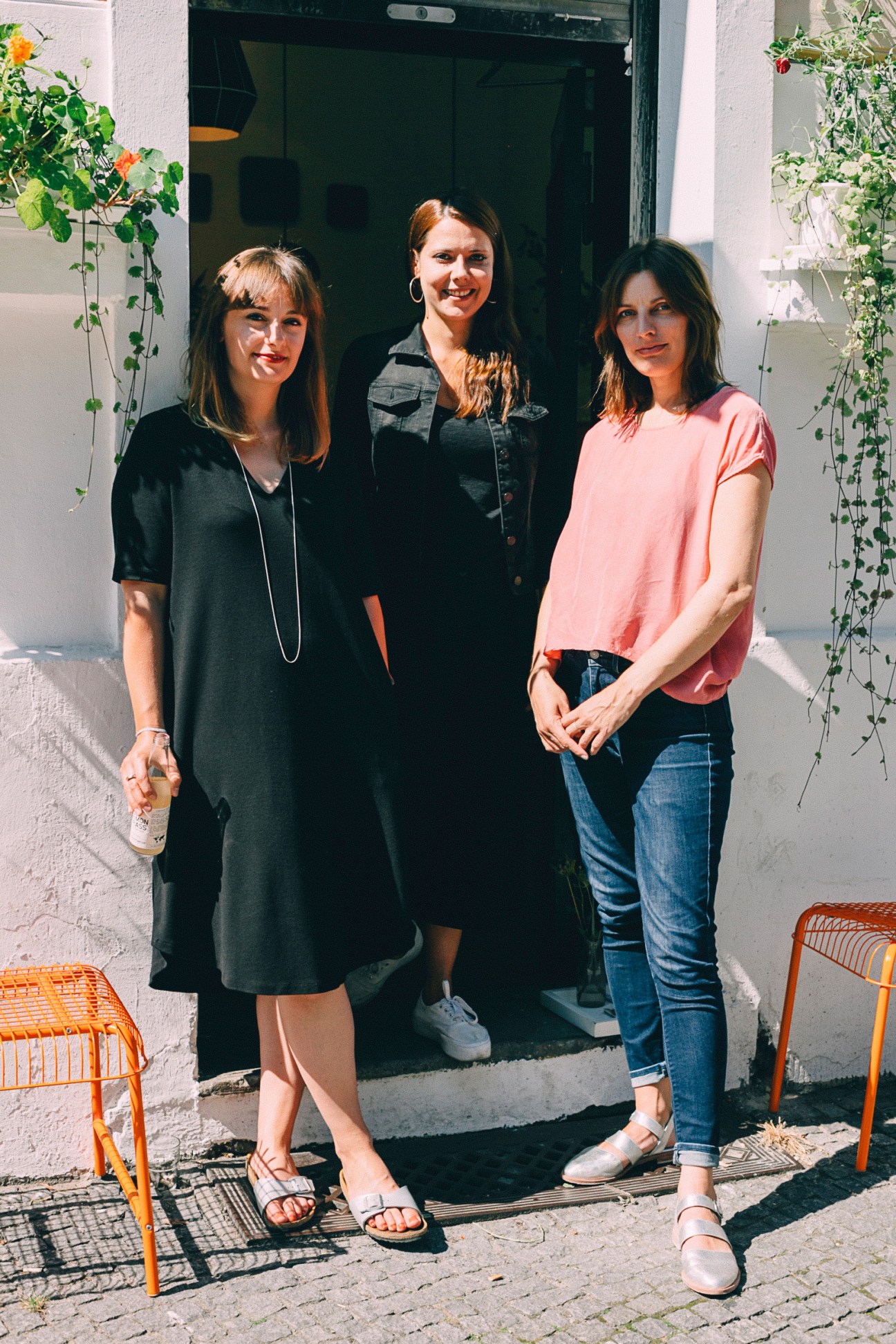 Three women standing in a doorway with hanging plants, smiling at the camera.