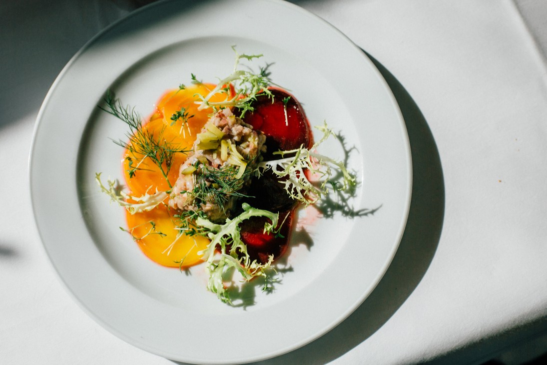 Matjes salad with sliced beetroot, herring, and fresh herbs on a white plate.