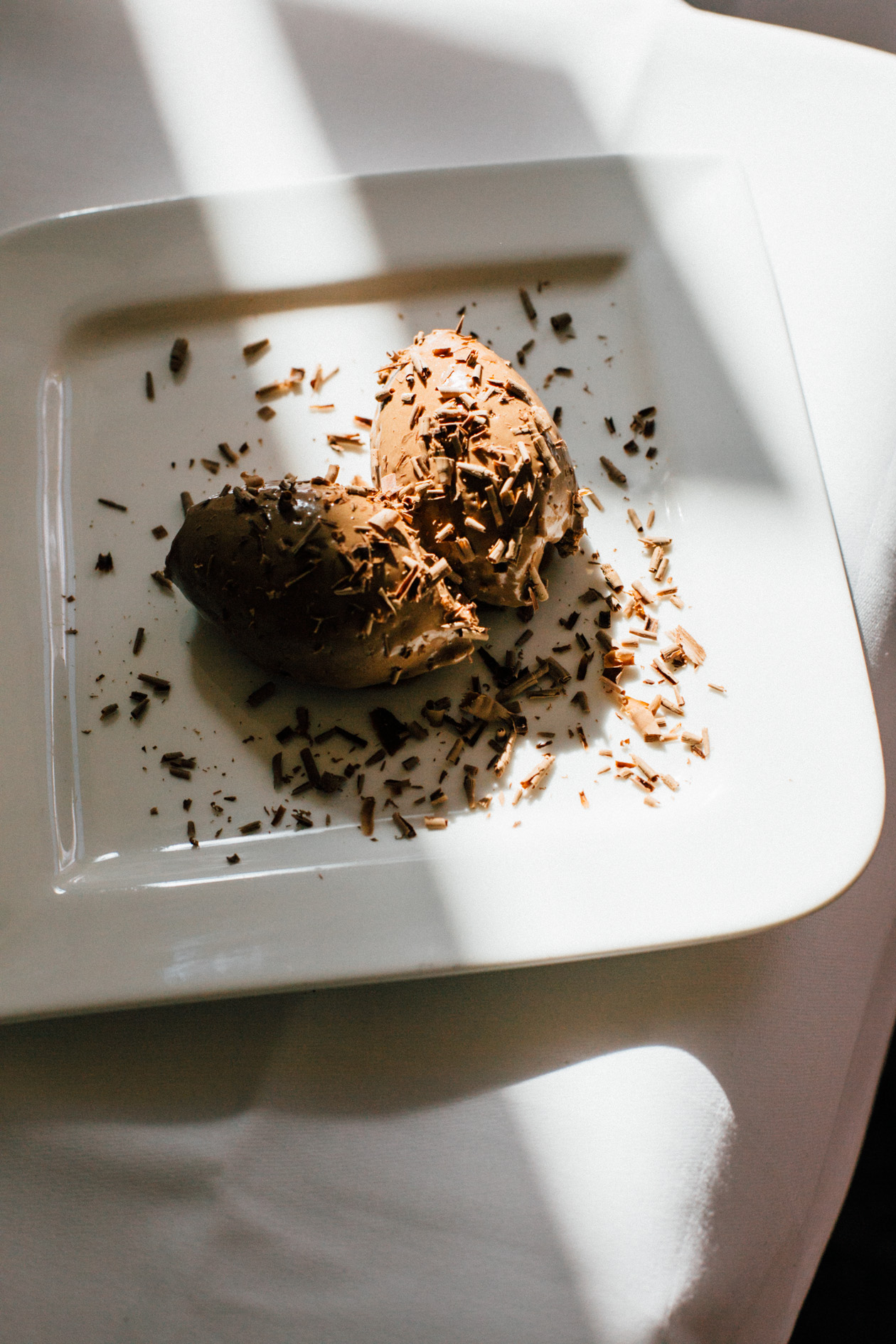 Mousse au chocolat dessert garnished with chocolate shavings on a white square plate.