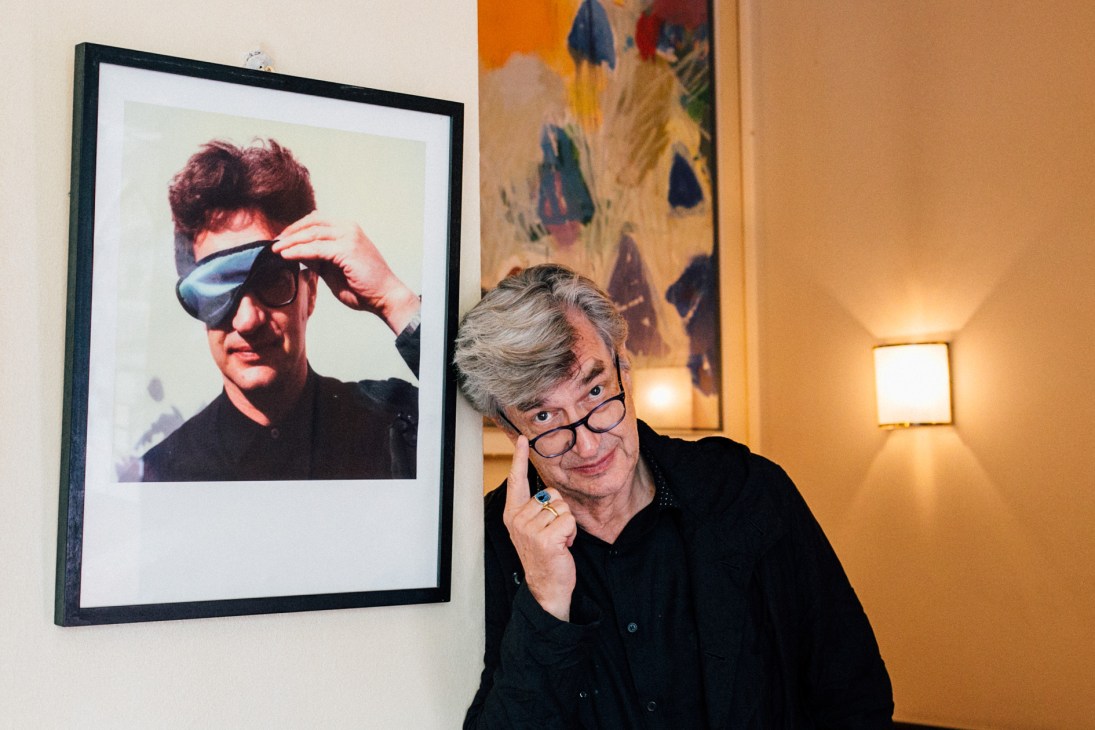 Wim Wenders poses next to a framed photograph of his younger self at Florian restaurant in Berlin.