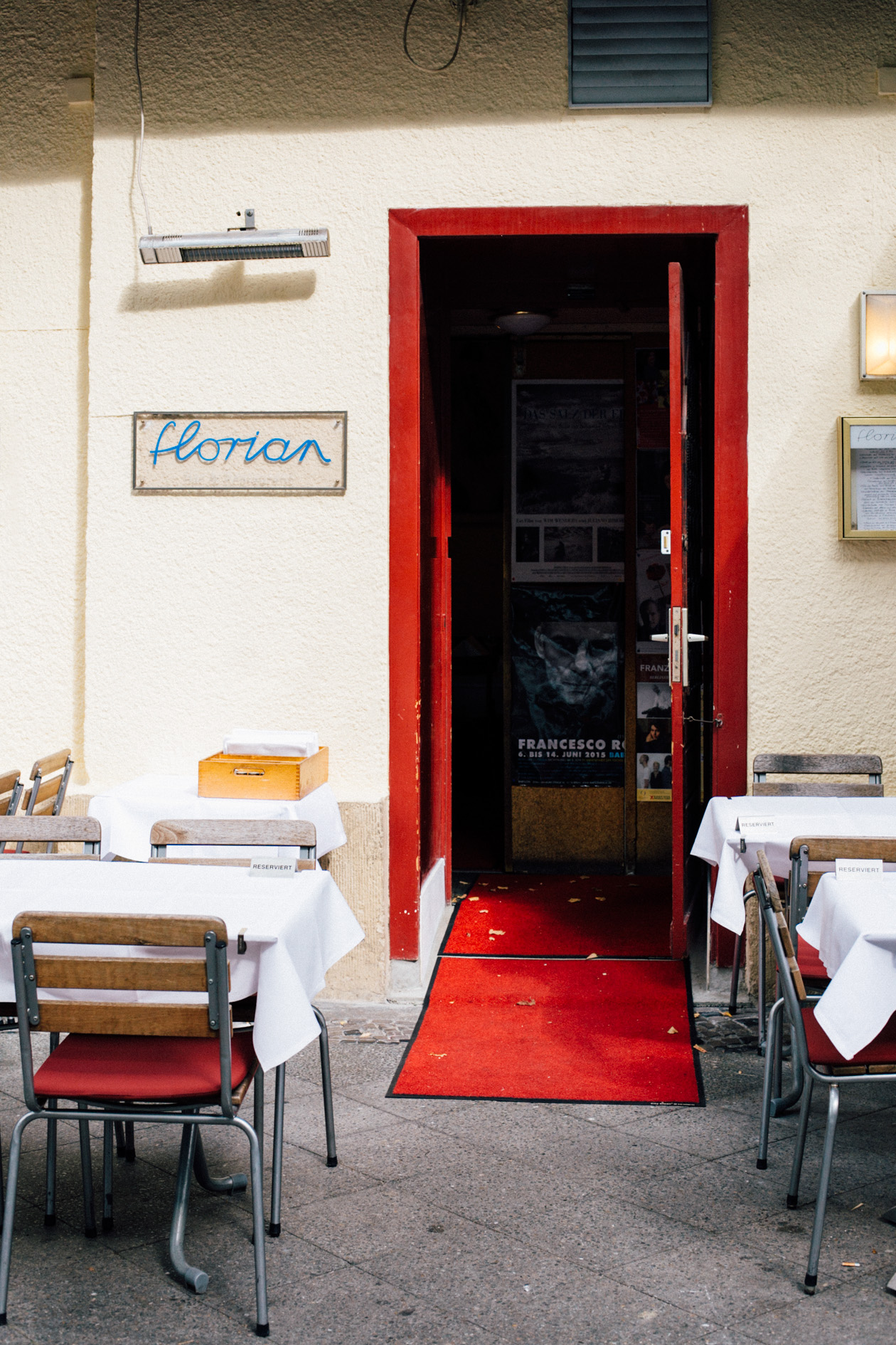 The entrance to Florian restaurant with a red door frame and blue "Florian" sign on a cream-colored wall.