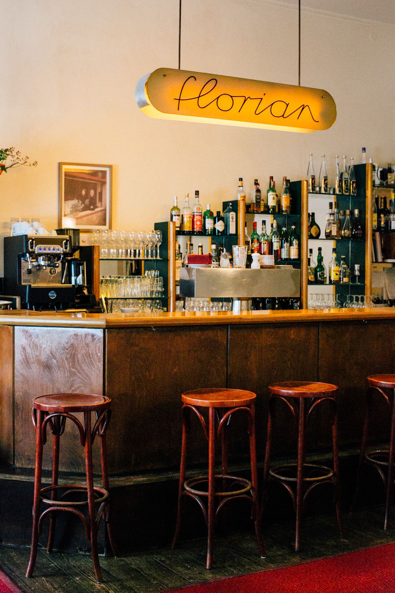 Florian restaurant bar with illuminated sign, bottles, and bentwood stools.