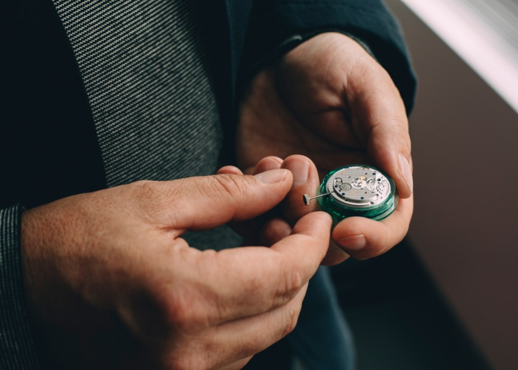 Hands holding an open Nomos Glashütte watch movement showing its internal mechanism and dial.