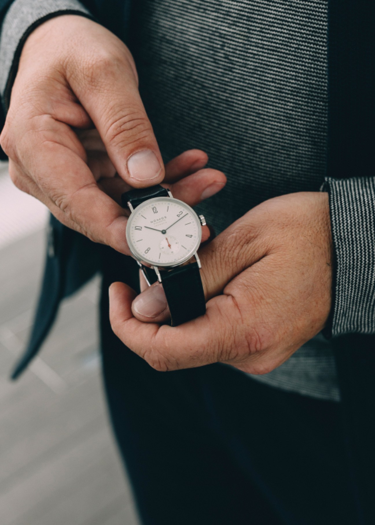 Person holding a Nomos watch with white dial and black leather strap on their wrist.