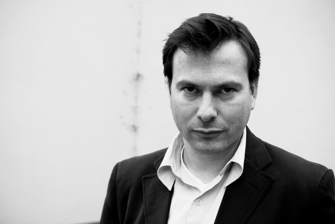 Black and white portrait of Simon Anholt, a man with dark hair wearing a black blazer and white shirt against a plain background.