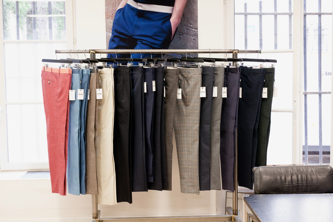 A person standing above a rack of Bernard Zins trousers in various colors and fabrics displayed on hangers.