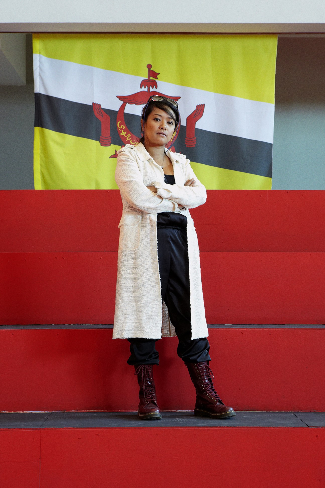 Film director Siti Kamaluddin stands with arms crossed in front of the Brunei flag.