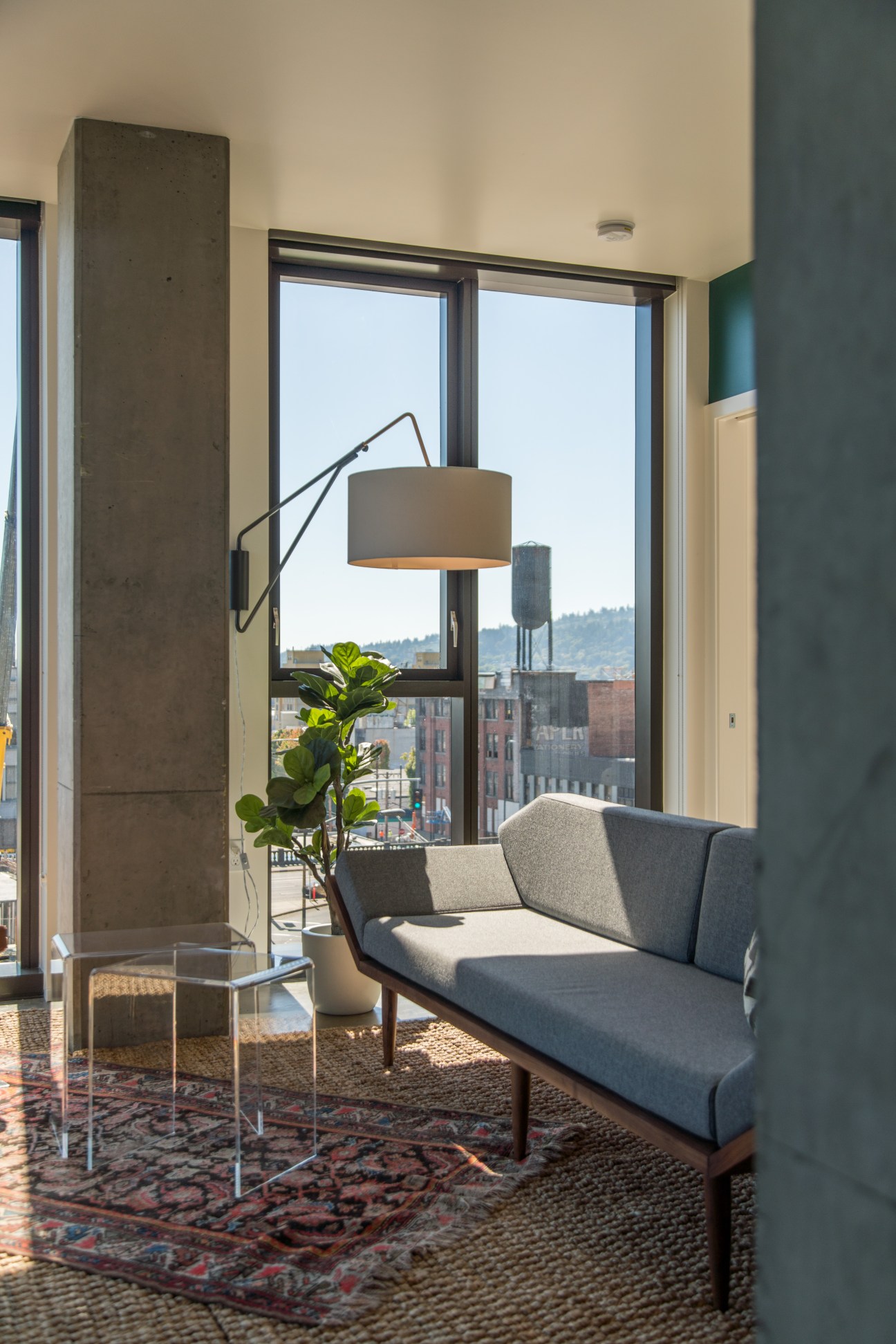 Modern apartment interior with gray sofa, floor lamp, and large windows overlooking Portland cityscape
