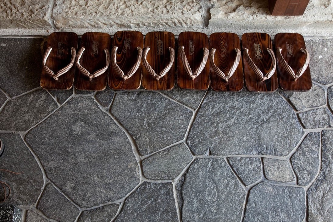 Eight pairs of traditional wooden geta sandals with white fabric straps lined up on stone flooring.