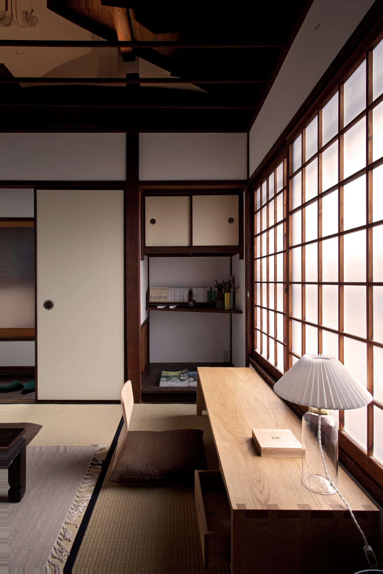 Japanese study room with tatami mat flooring, wooden desk, paper lantern lamp, sliding lattice windows, and built-in shelving.