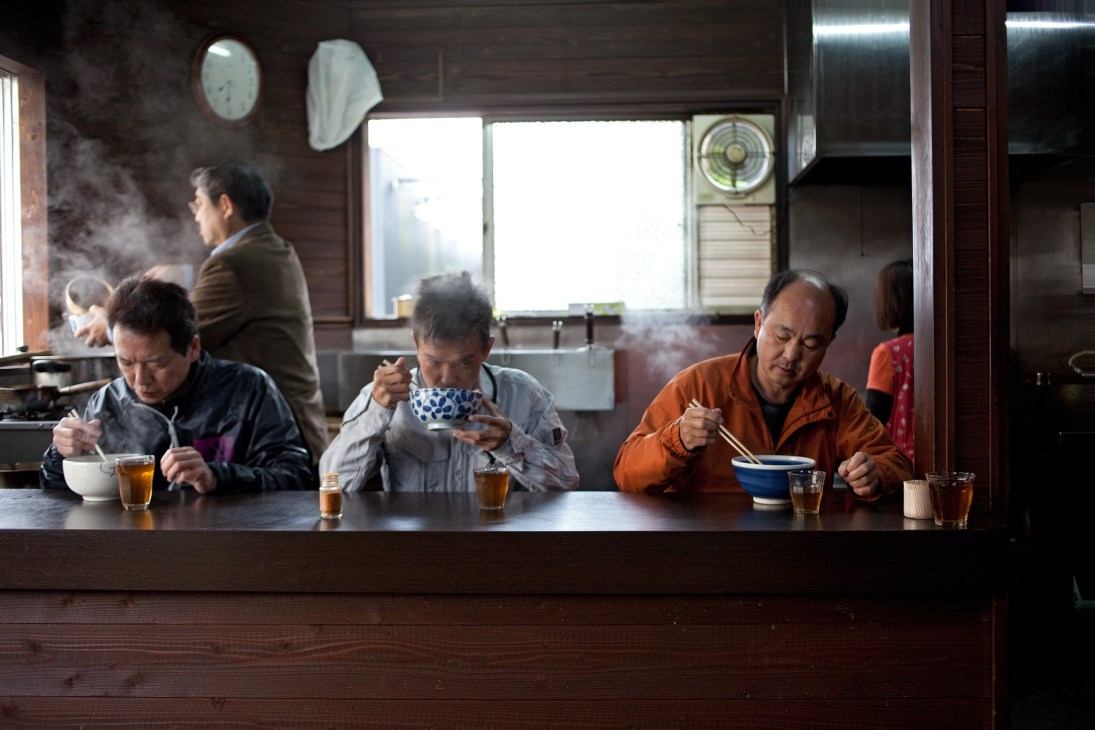 Locals eating udon noodles at a counter at Yamako Udon restaurant in Uwajima, Japan.