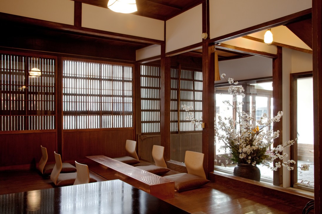 Interior of Kiya Ryokan's café space with traditional wooden lattice windows, sliding screens, wooden flooring, and a floral arrangement.