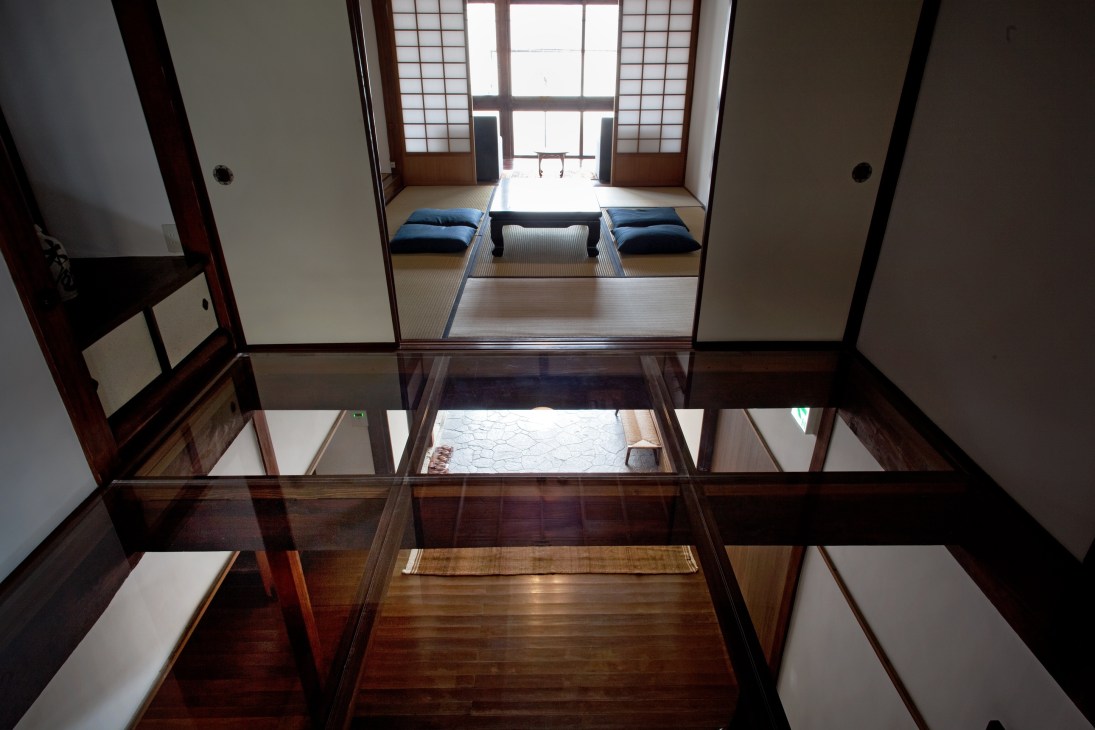 Interior view of Kiya Ryokan showing transparent acrylic floor panels revealing traditional tatami mats and wooden structures below.