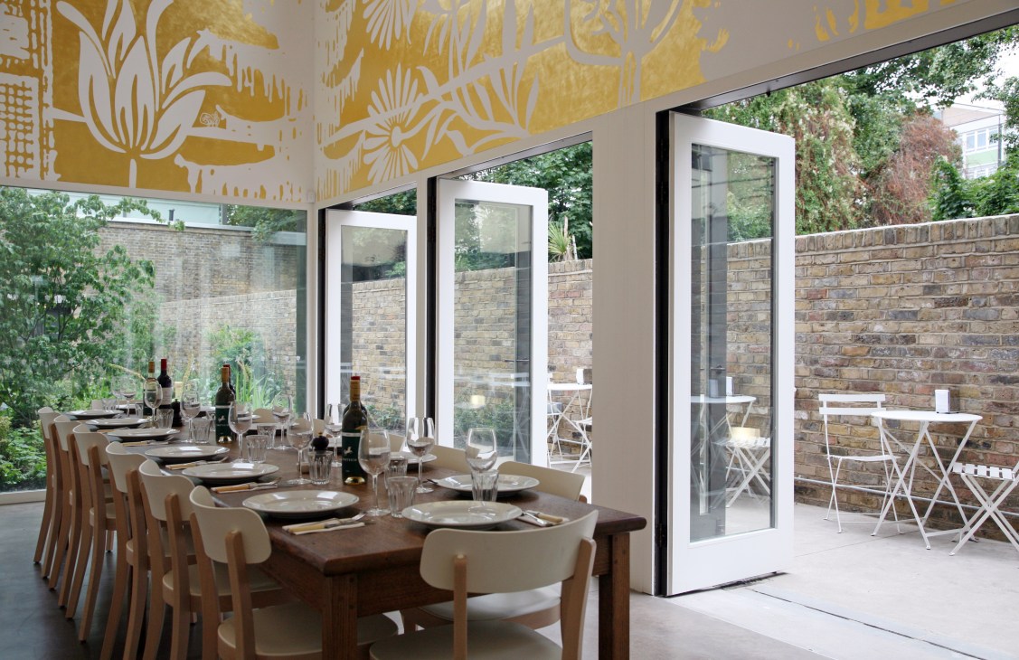 Modern dining room at No67 cafe with long table, wooden chairs, and gold patterned ceiling overlooking brick courtyard.