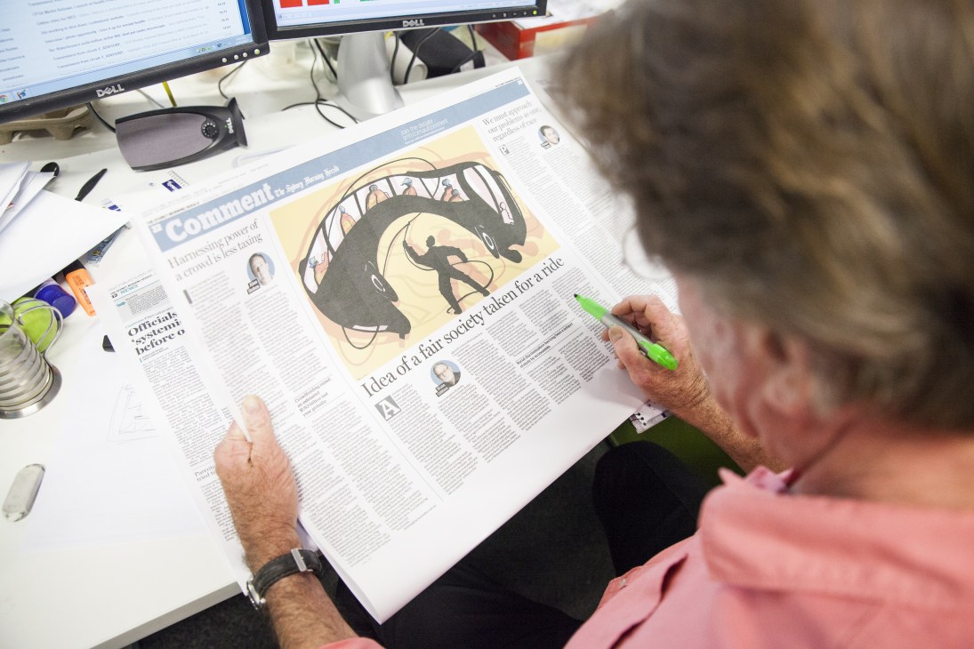 Editor reviewing the Sydney Morning Herald newspaper at desk with computer and office supplies.