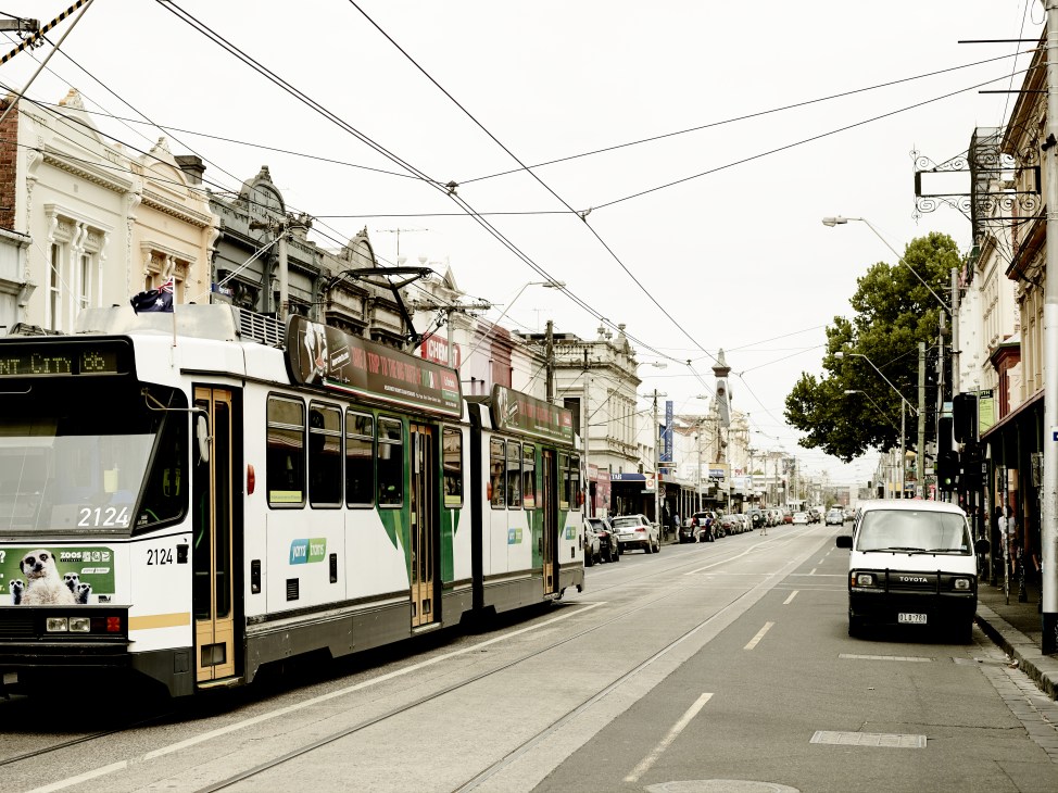 A Melbourne tram travels along Smith Street in Collingwood, lined with historic buildings and parked cars.