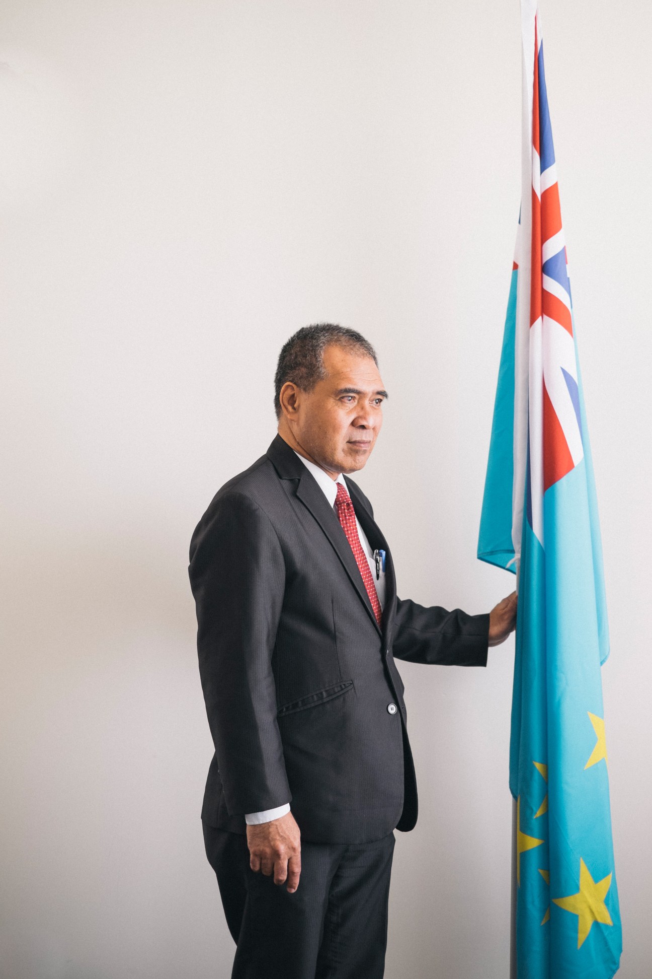 Minute Alapati Taupo, Tuvalu's ambassador to Taiwan, in formal business attire beside the Tuvalu flag.