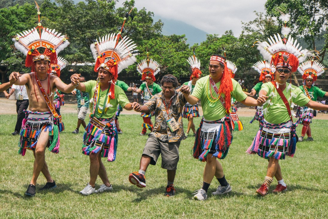 Amis aboriginal tribe members in traditional red and white headdresses dance with a visitor at a cultural event in Taipei.