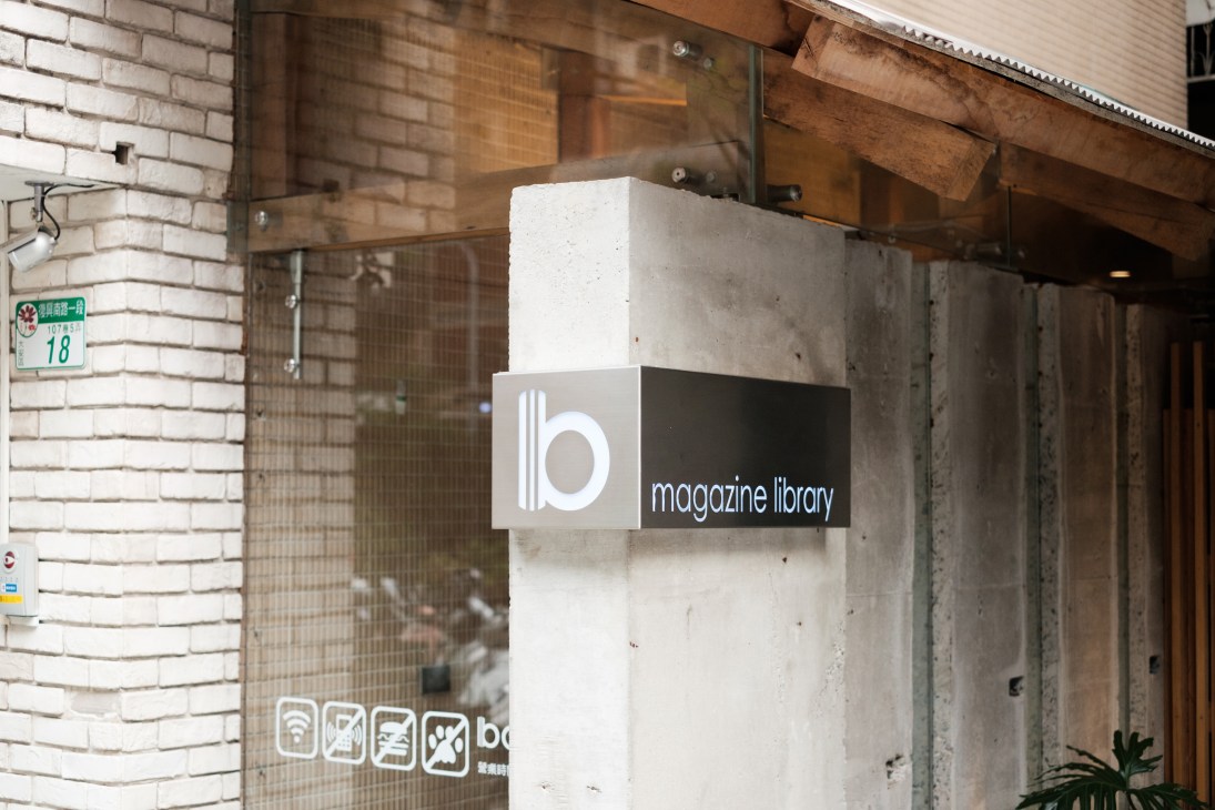 Exterior storefront with 'Boven magazine library' signage mounted on white and black panel above entrance.