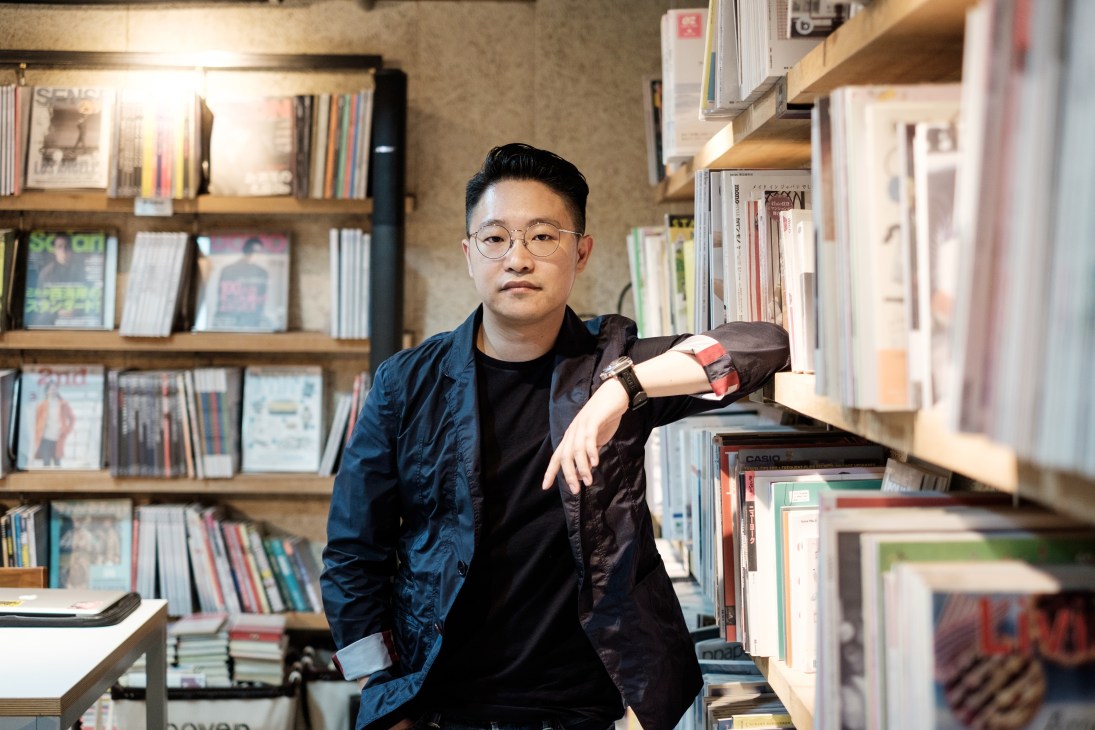 Producer Johnason Lo leans against shelves in the Boven magazine library wearing glasses and a dark jacket.