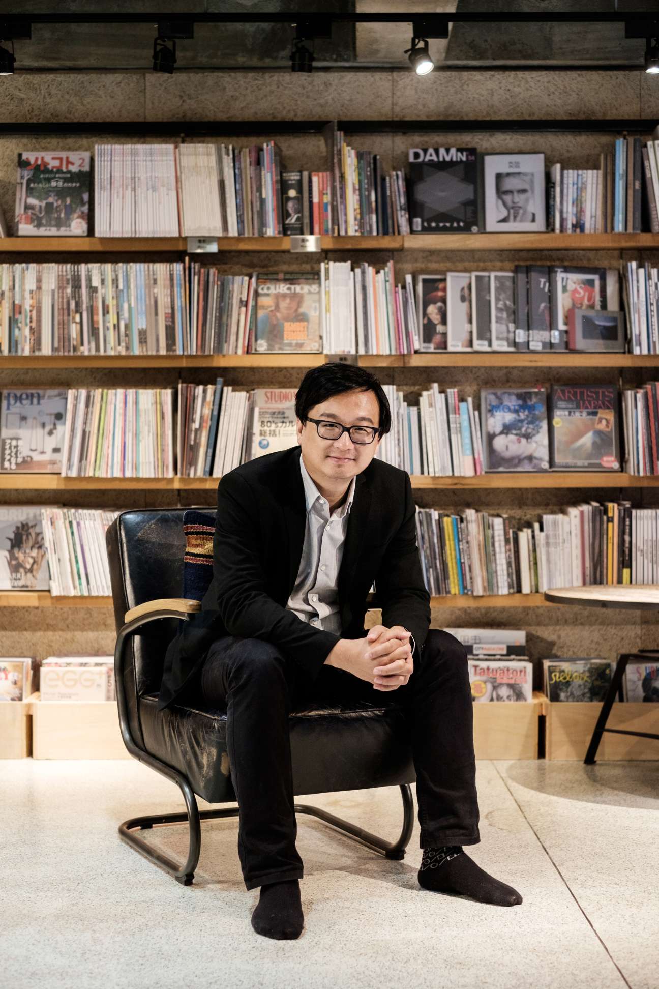 Host Chang Tieh-chih sitting in a black leather chair against shelves of magazines and publications