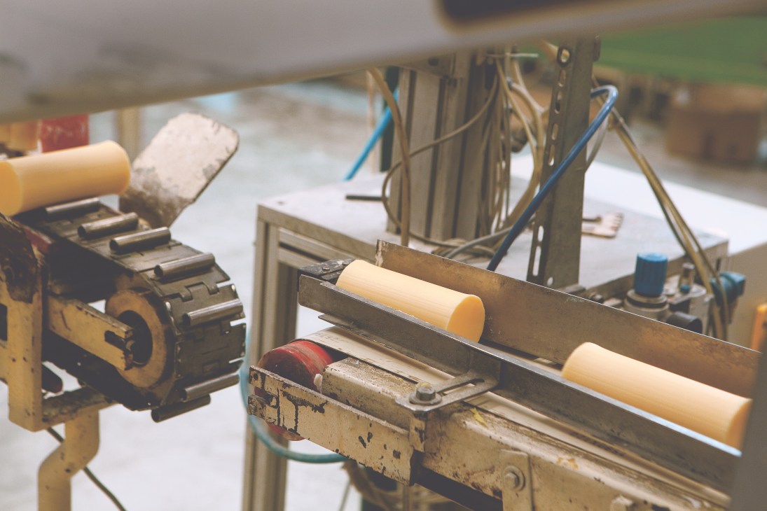 Freshly made soap bars being cut on a mechanical assembly line machine.