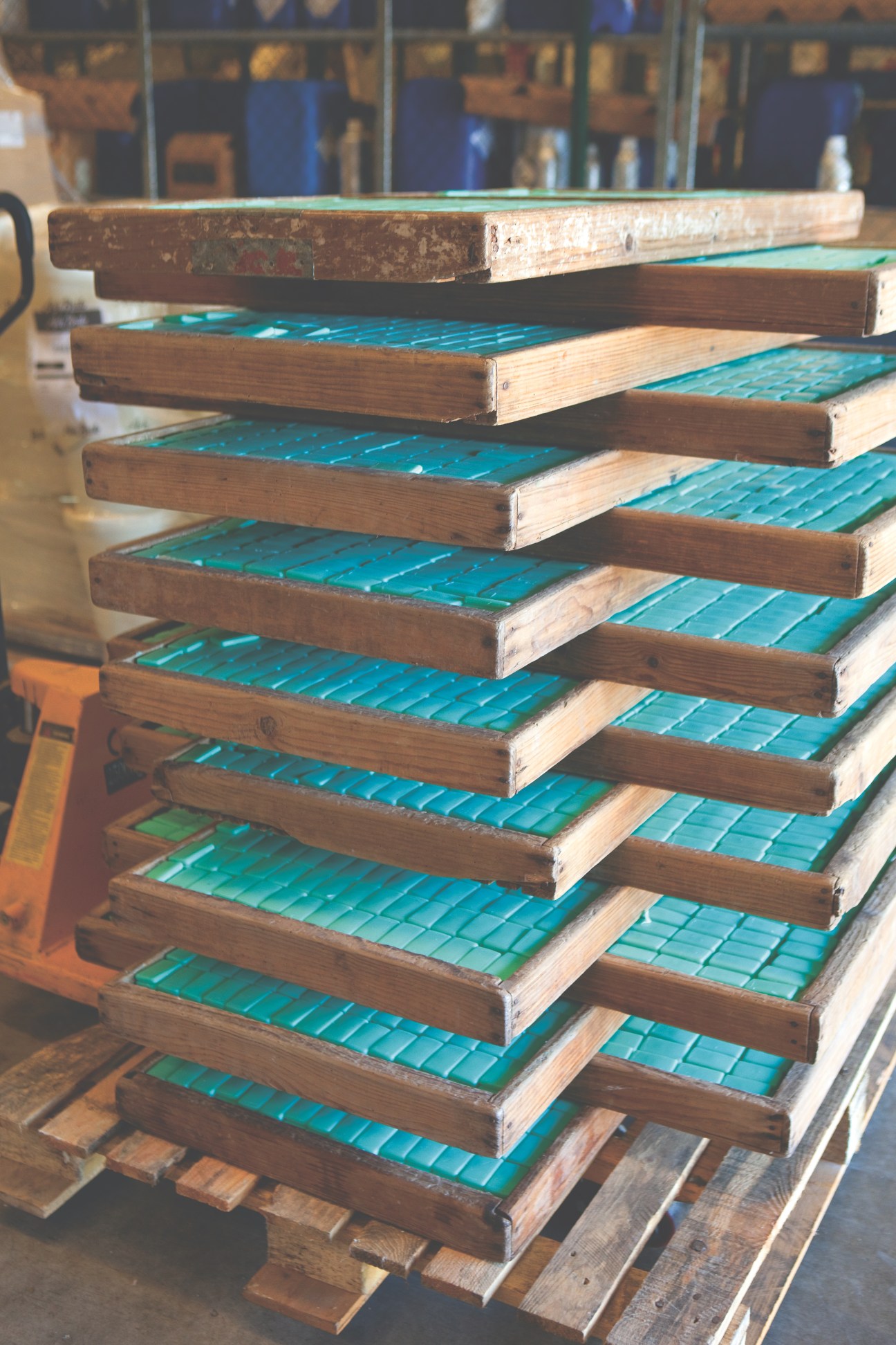 Stacked wooden drying racks with turquoise-colored soap bars arranged in rows.