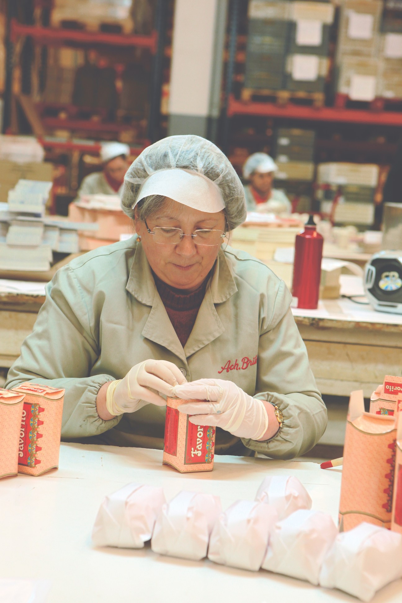 Woman in protective gear packaging Ach. Brito Claus Porto soap boxes on factory floor.
