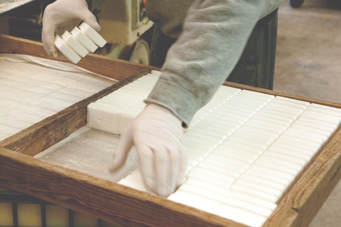 Worker arranging freshly cut white soap bars on wooden drying racks.