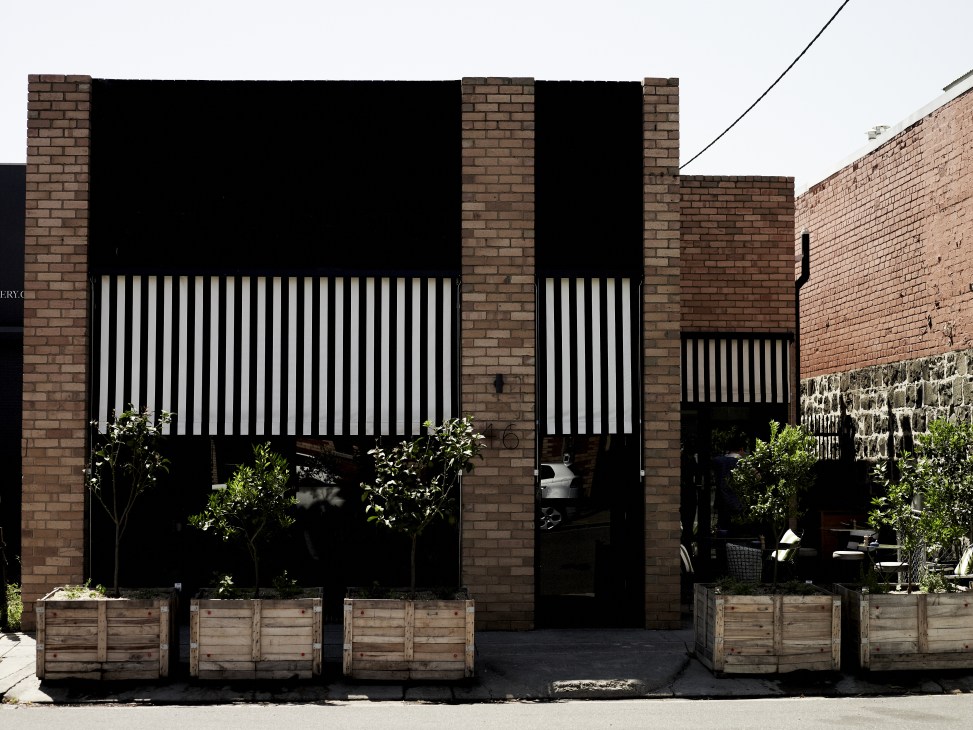 Modern brick warehouse café with black vertical striped panels, wooden planters and plants outside.