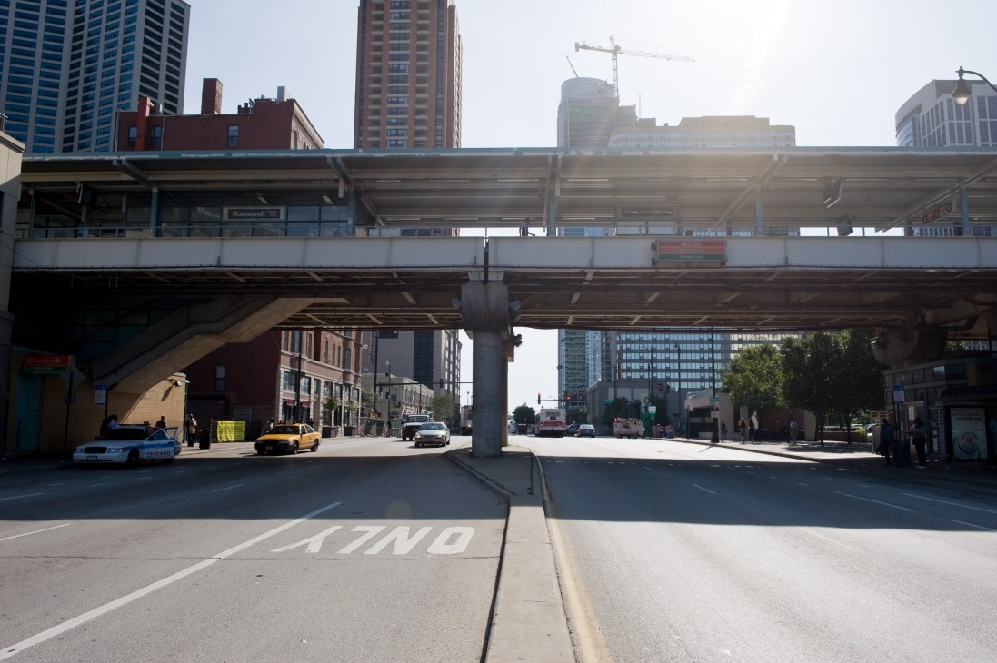 Chicago's elevated 'L' railway station with Roosevelt platform sign above a street with buildings and taxi.