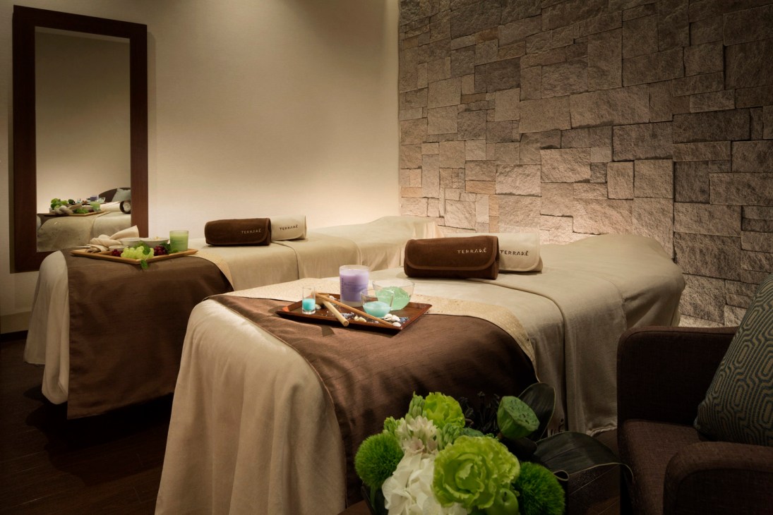 Spa treatment room with massage beds, stone wall, mirror, and fresh flowers at Spa Tokione.