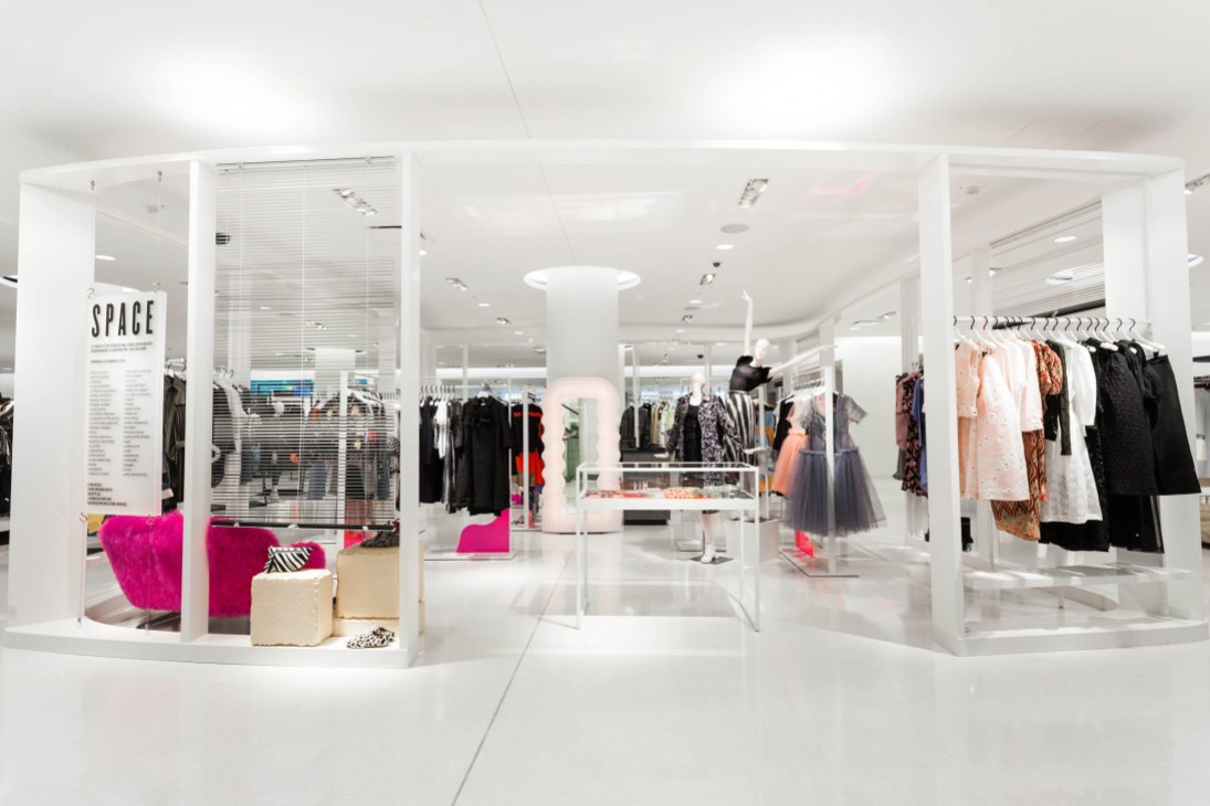 Interior view of Nordstrom's Space boutique featuring white minimalist design with clothing displays and bright pink accent seating.