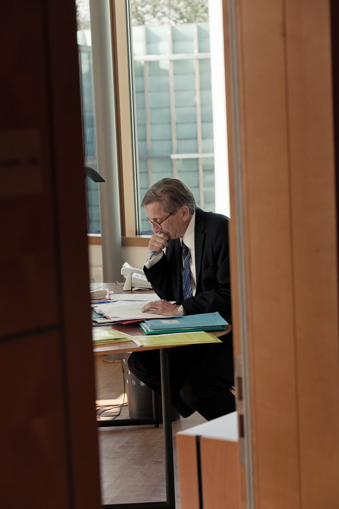 Swedish ambassador Staffan Carlsson sits at a desk reviewing documents in an office with large windows.