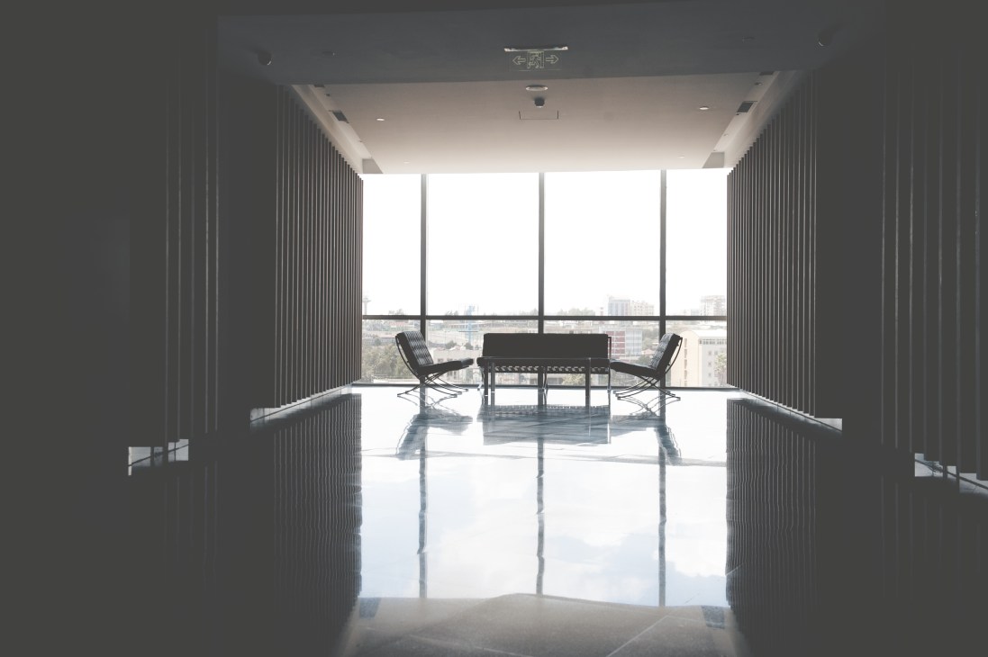 Modern high-rise office interior with Barcelona chairs, reflective white floor, and city views.