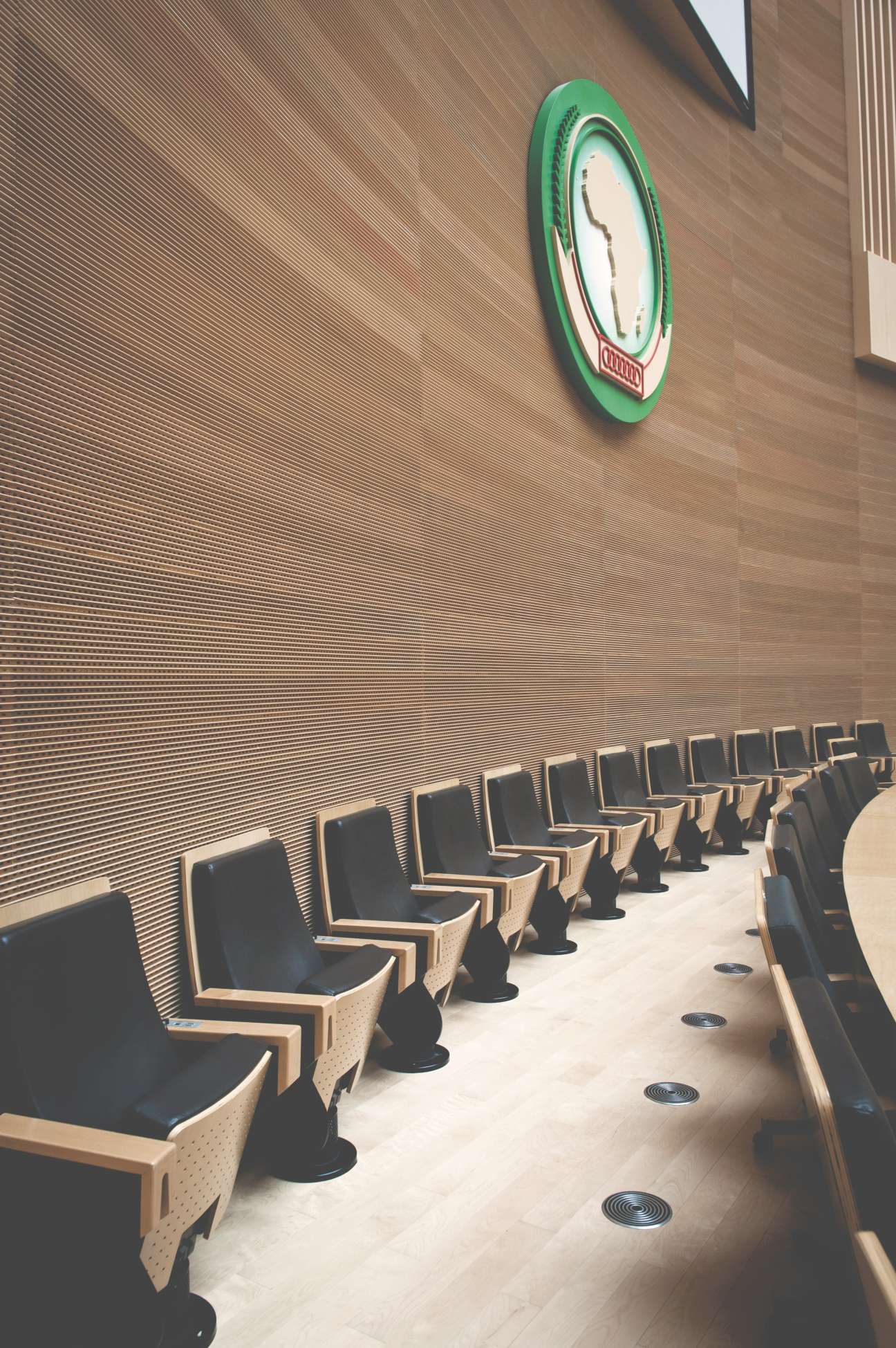 Row of modern chairs in a plenary hall with an African Union crest clock on the wall.