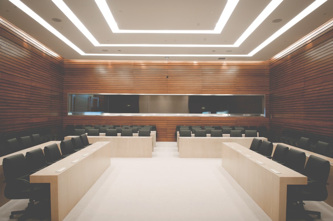 Modern conference room with wooden walls, light ceiling panels, and two long white tables with dark chairs on either side.
