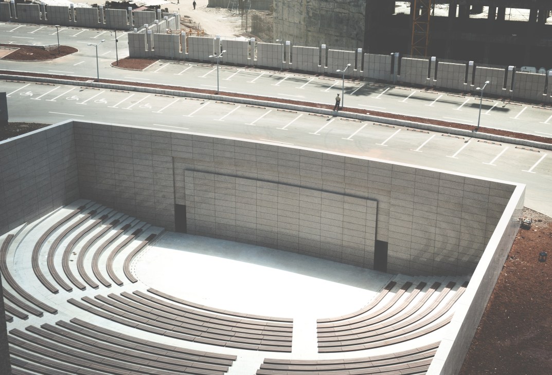 Aerial view of an empty concrete outdoor amphitheatre with curved seating under construction.
