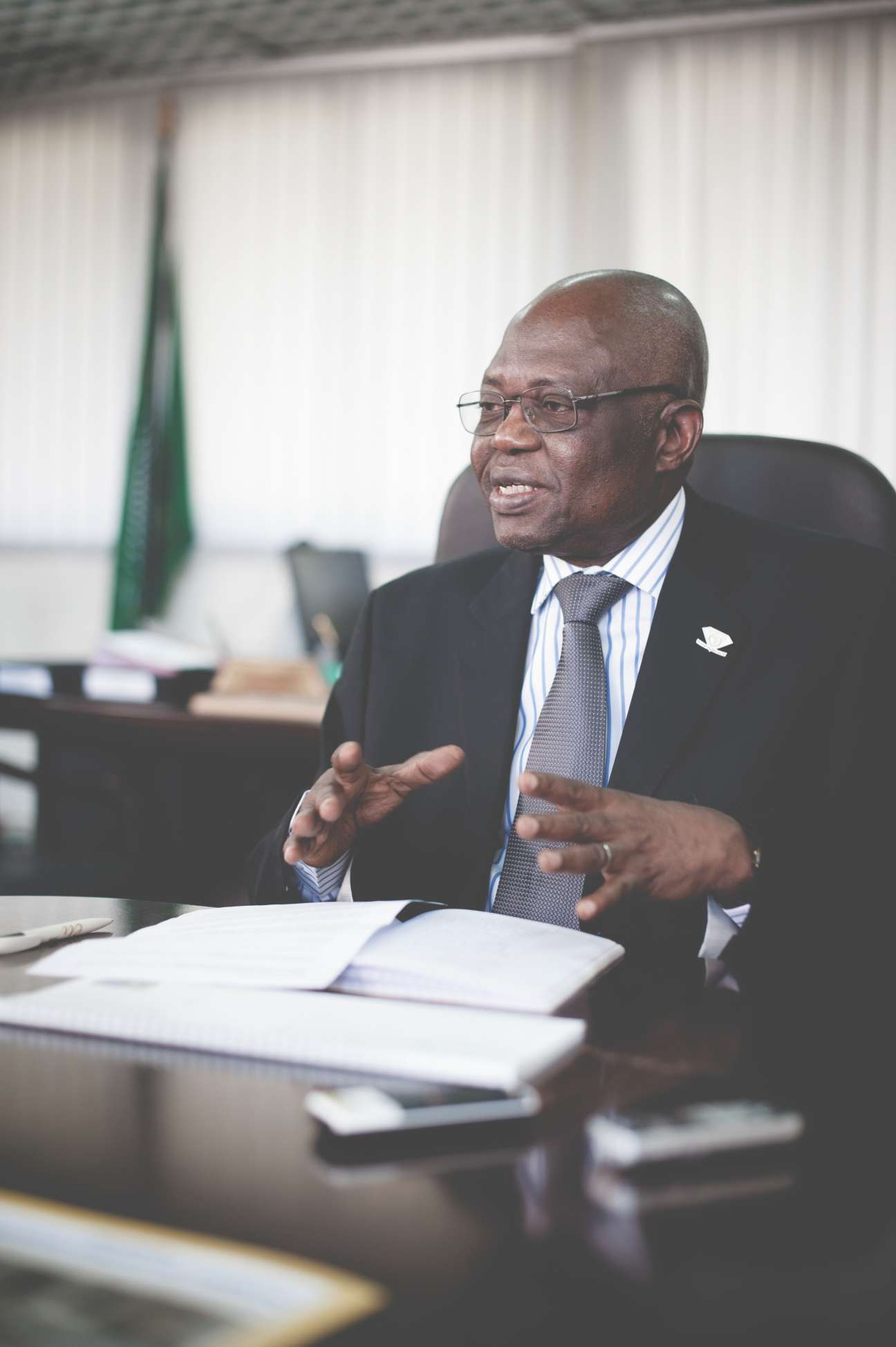 AU commissioner Jean Ezin speaks at his desk in an office with an African Union flag in the background.