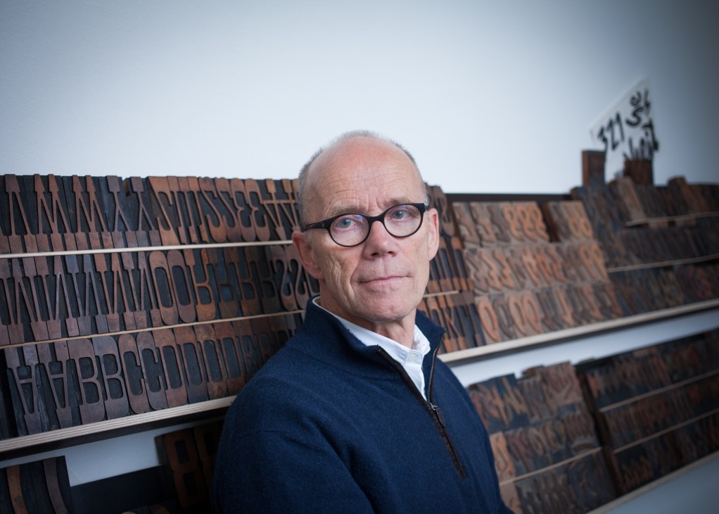 Erik Spiekermann stands in front of wooden letterpress type sorted in shelves at his P98a workshop in Berlin.