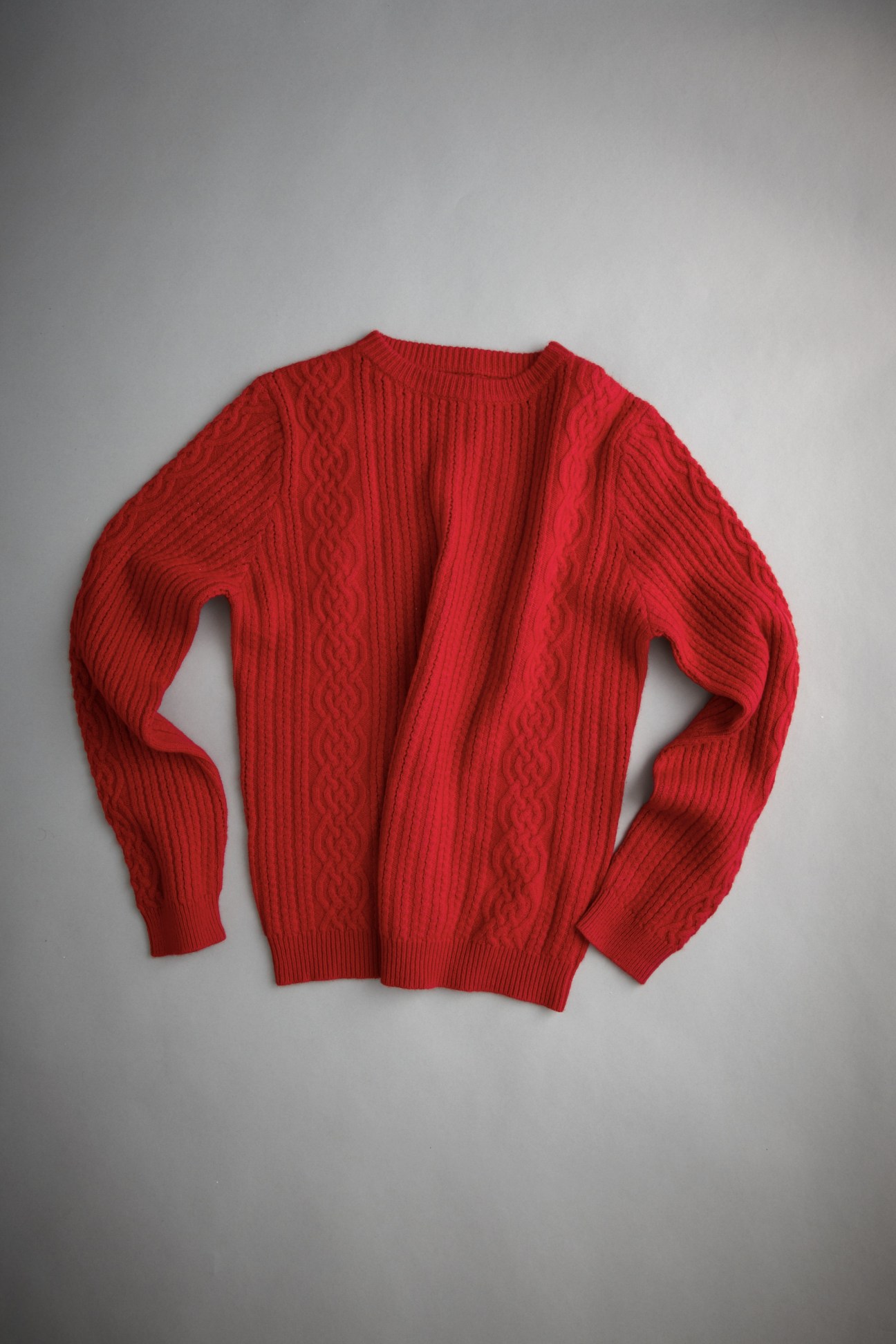 Red cashmere cable knit crew neck sweater laid flat against a gray background.