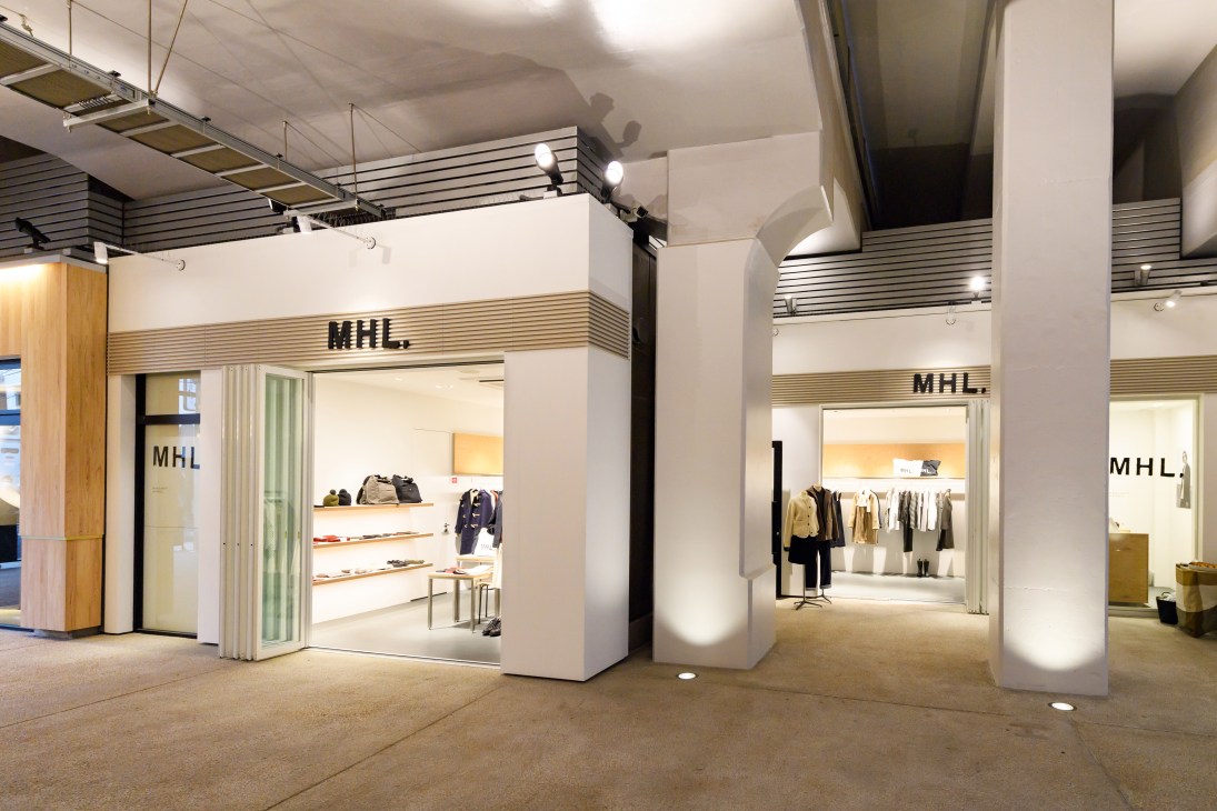 Margaret Howell shop interior under train tracks with minimalist white storefront and clothing displays.