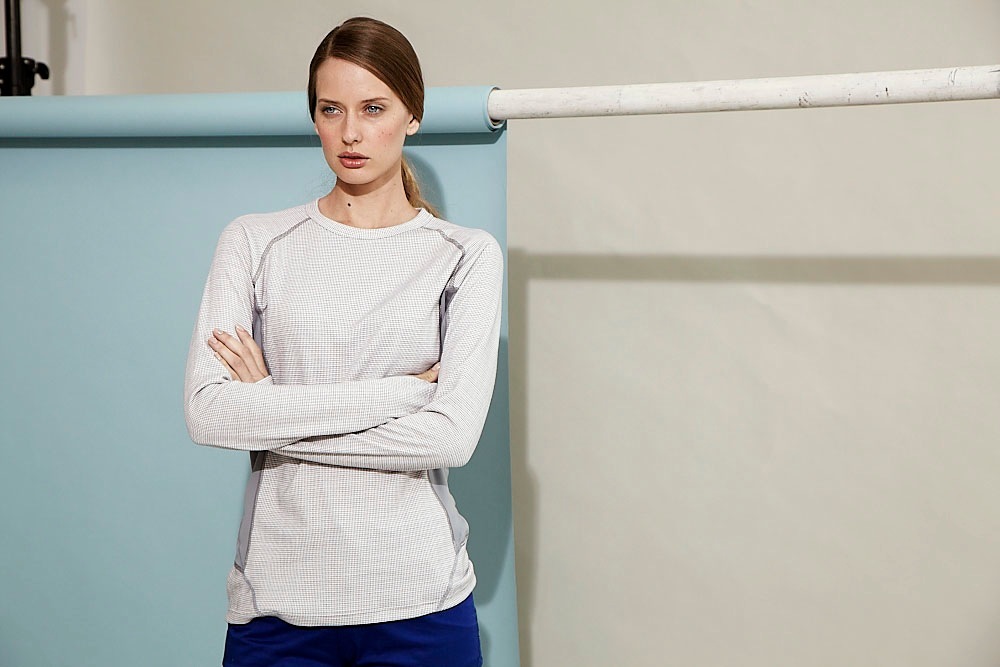 Woman wearing a light gray long-sleeve thermal shirt and navy pants against a blue and white background.