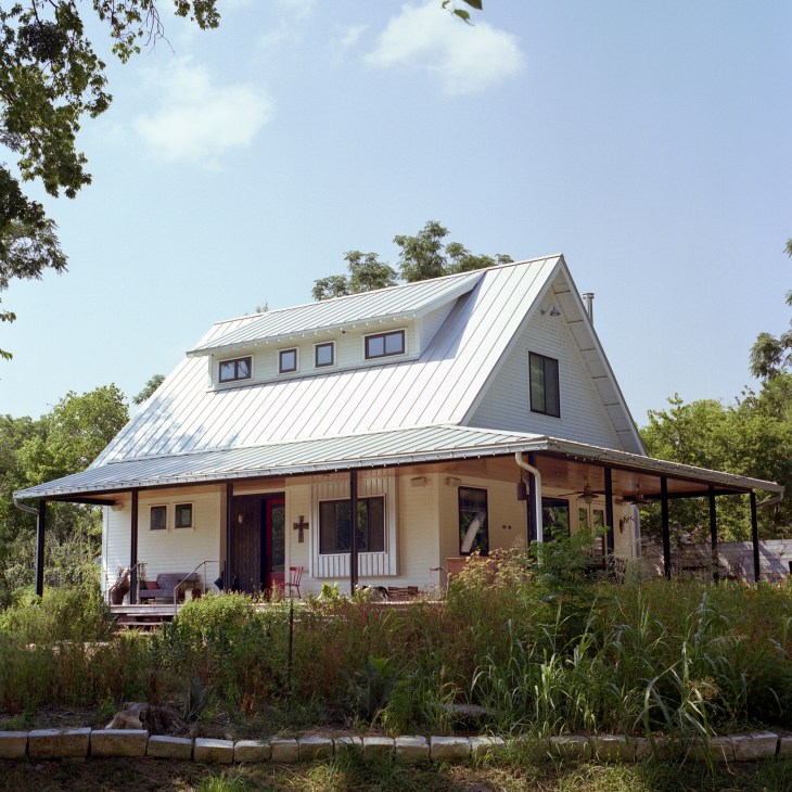 Modern farmhouse with metal roof and wrap-around porch surrounded by vegetation at Springdale Farm.