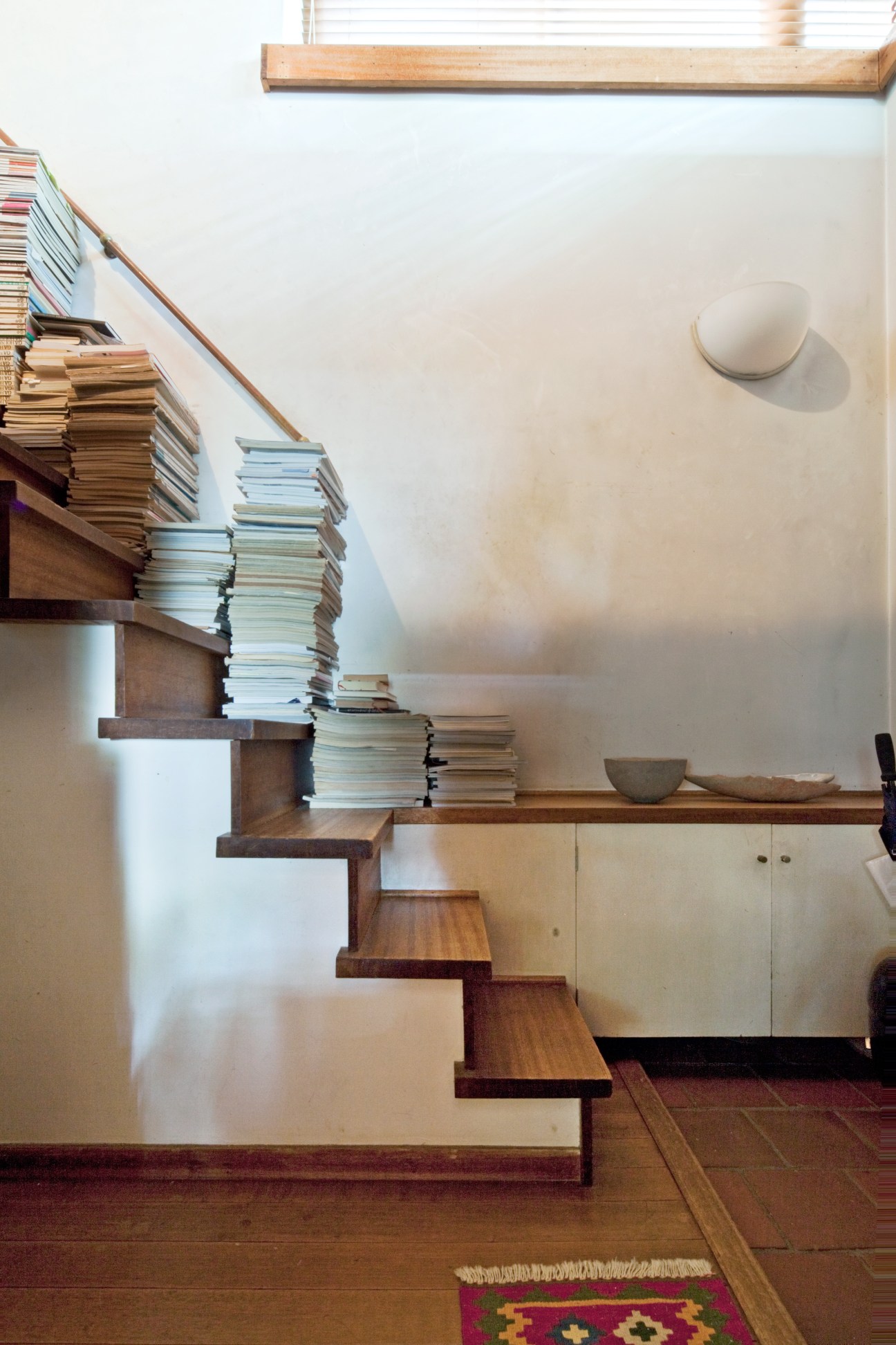 Modern wooden staircase with books stacked on each step and ceramic bowls on counter below