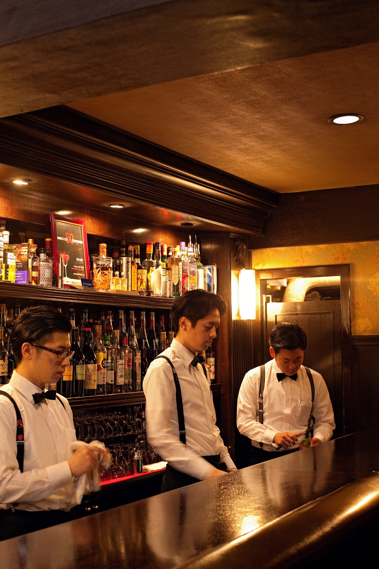 Three Japanese bartenders in white shirts and bow ties stand behind a polished bar at Star Bar Ginza.